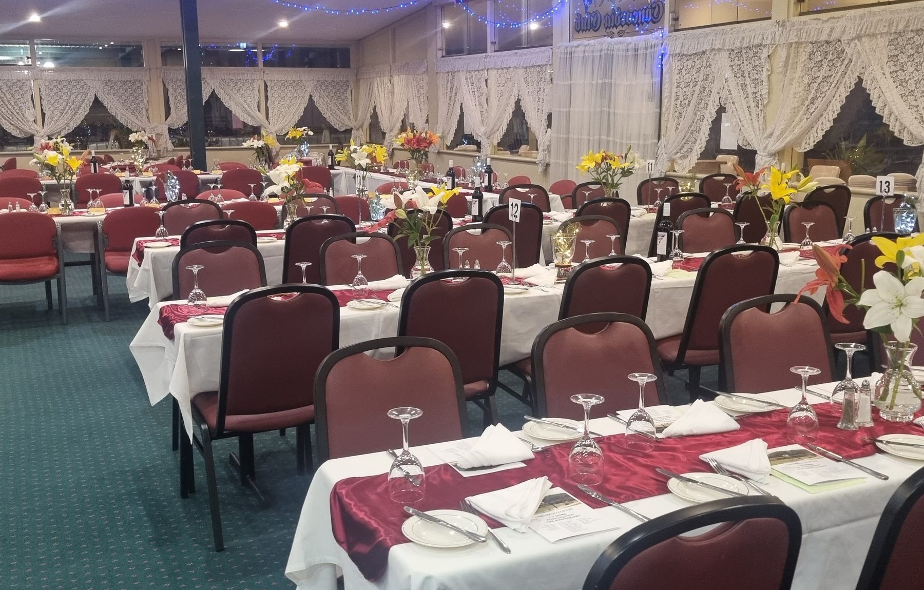 The Concordia Club function room set for an evening dinner, tables dressed in white linen and deep red runners